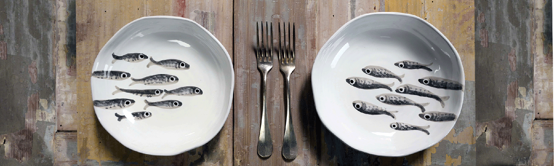 piatti bianchi con disegni di pesci grigi e forchette su tavolo in legno