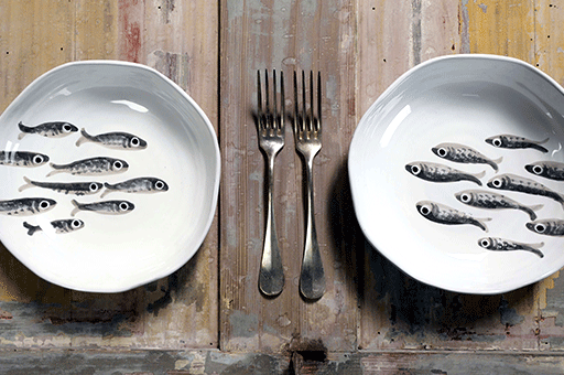 tavolo in legno vintage con due piatti pitturati a mano raffiguranti sardine e due forchette